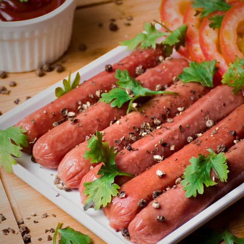 A close-up shot of grilled hotdogs garnished with parsley and pepper flakes.